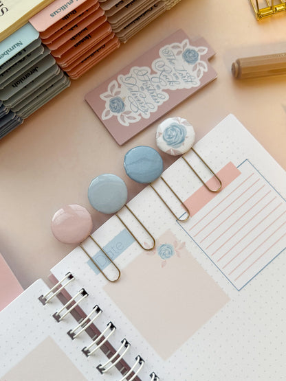 DotK Design Paperclip bookmarks being used in a journal. Each features shades of blue and pink with florals