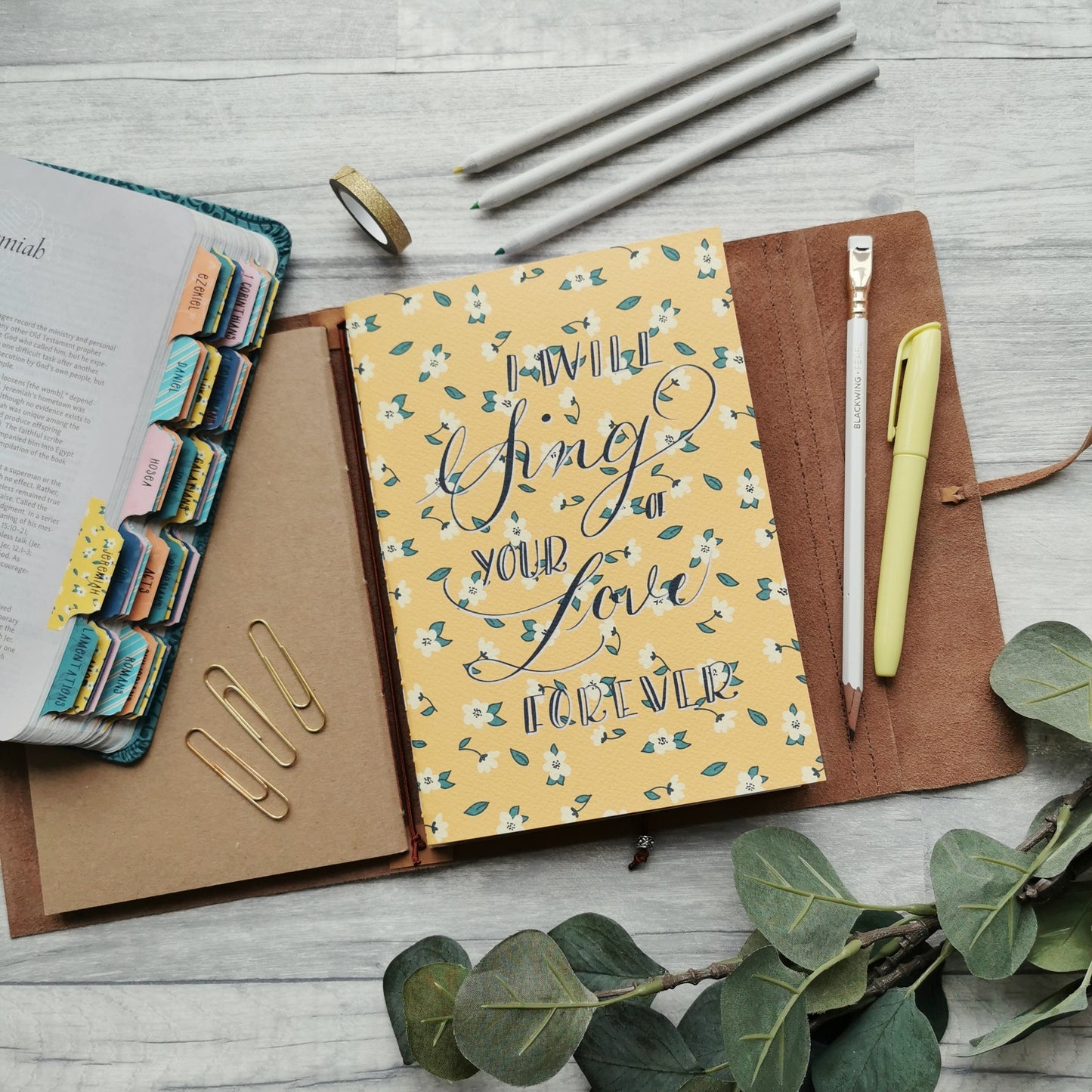 Christian prayer journal notebook in bright yellow with white daisy design and the word "I will sing of Your love forever" on the cover.